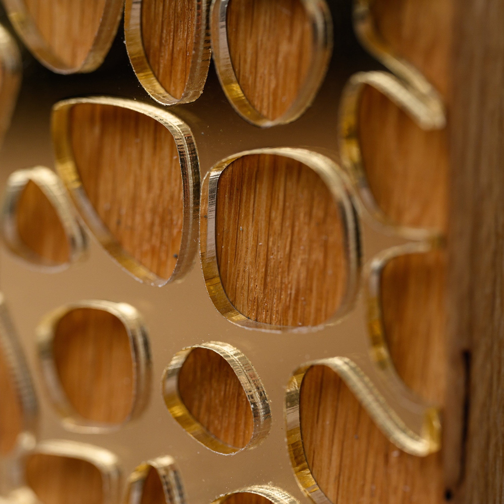 Macro detail of the polished gold acrylic cell pattern and the oak surface visible through it