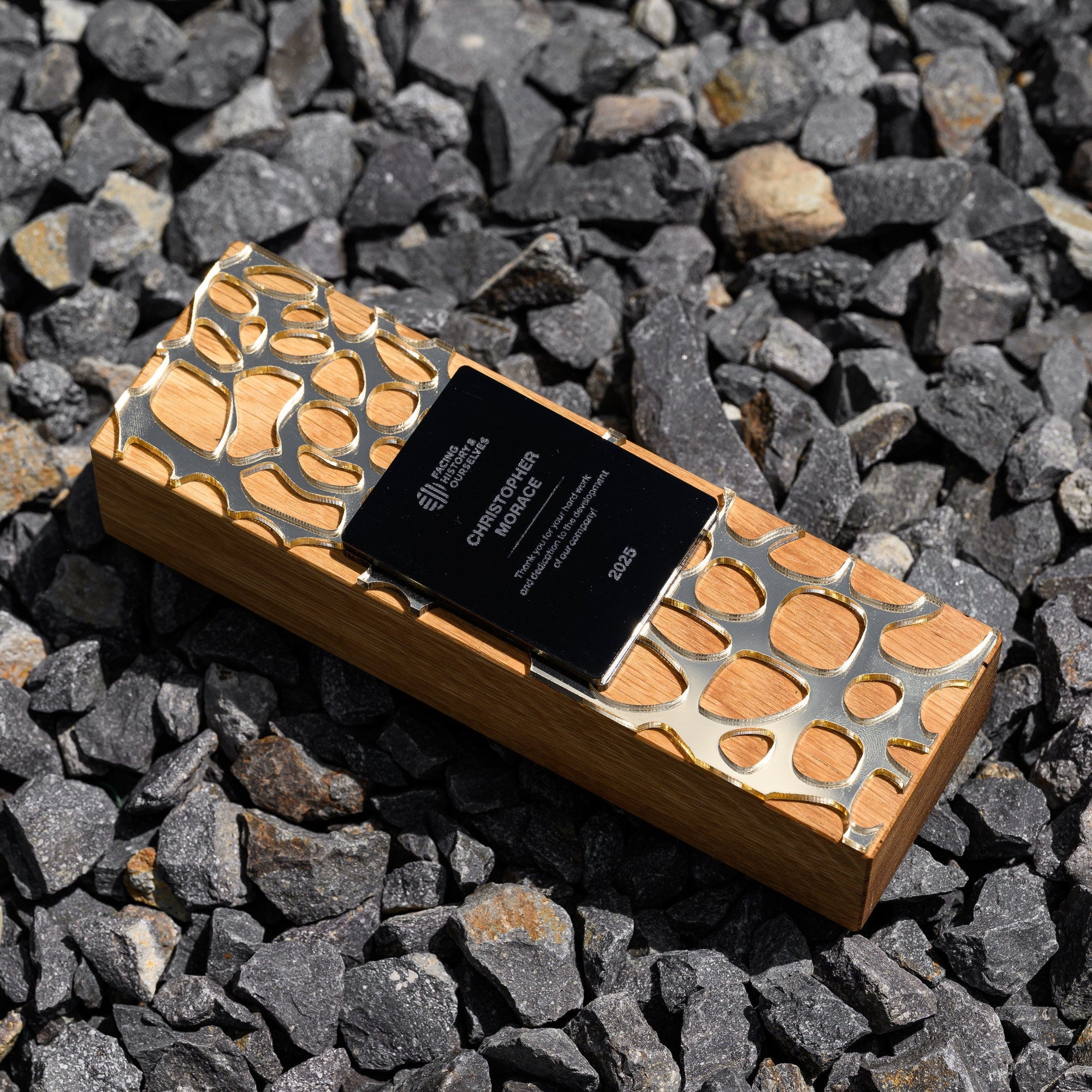 	Oak award with gold acrylic cut-out pattern lying on grey gravel with the engraved plate facing up