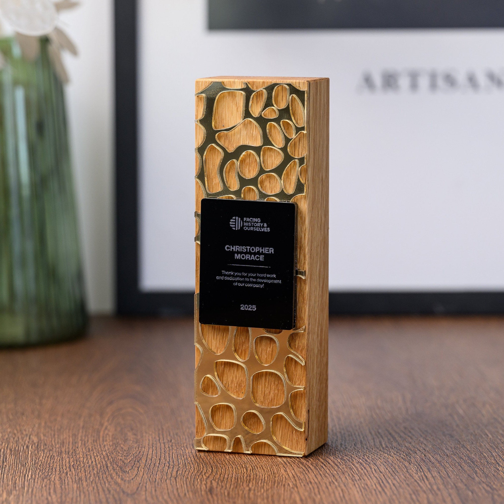 Custom oak and gold acrylic employee recognition award standing on a desk beside a green glass vase