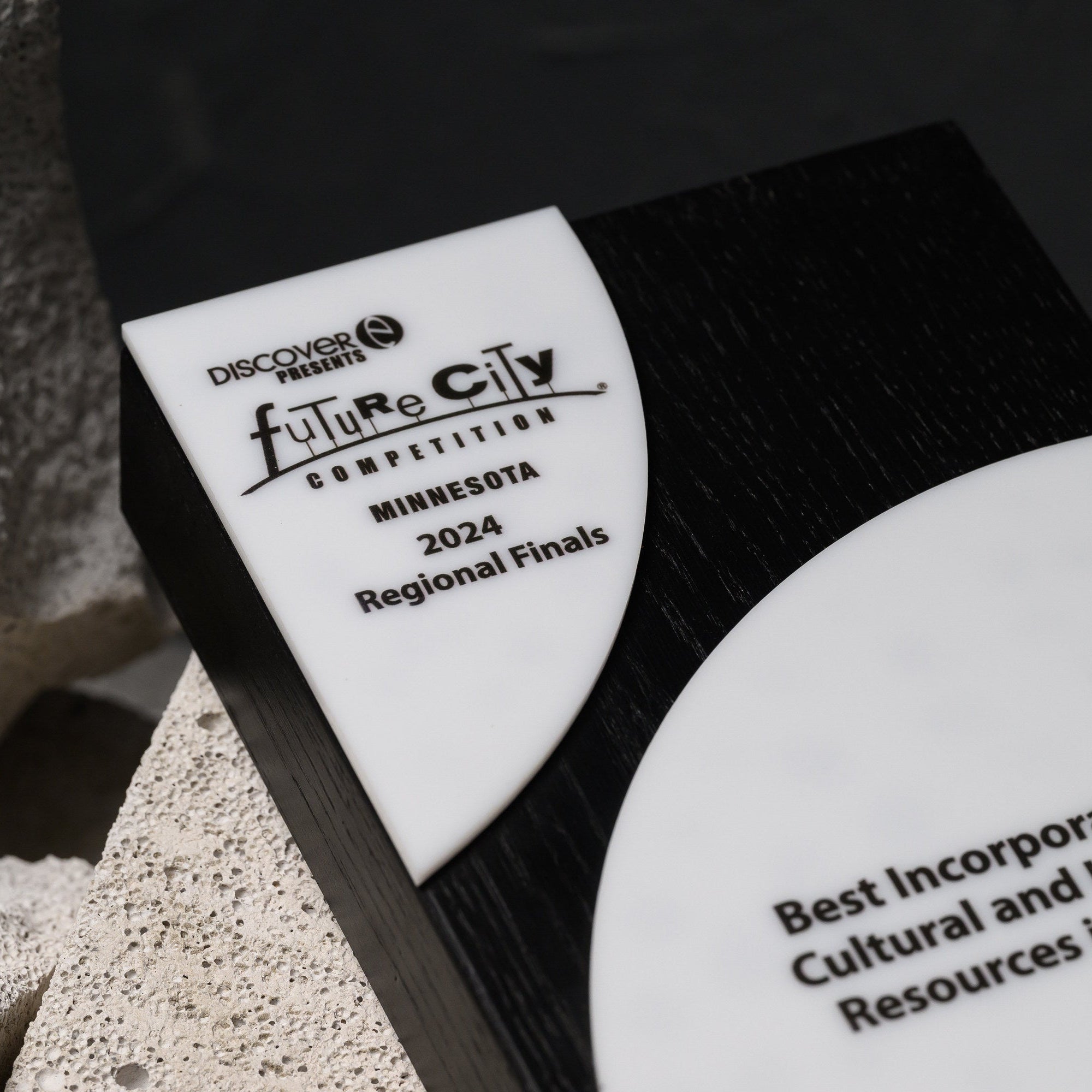 Award lying at an angle on stone, showing both printed panels against the dark wood