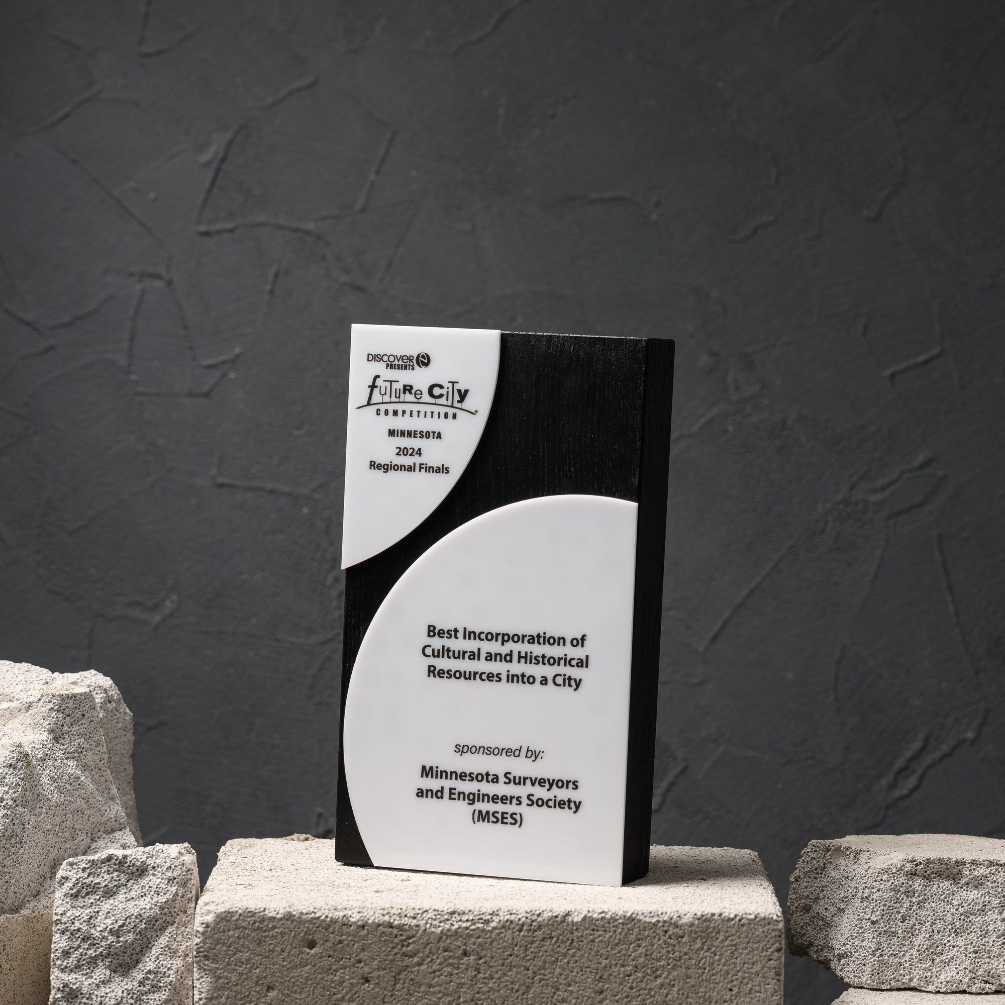 Blackened oak competition award with two white acrylic panels, on a stone plinth