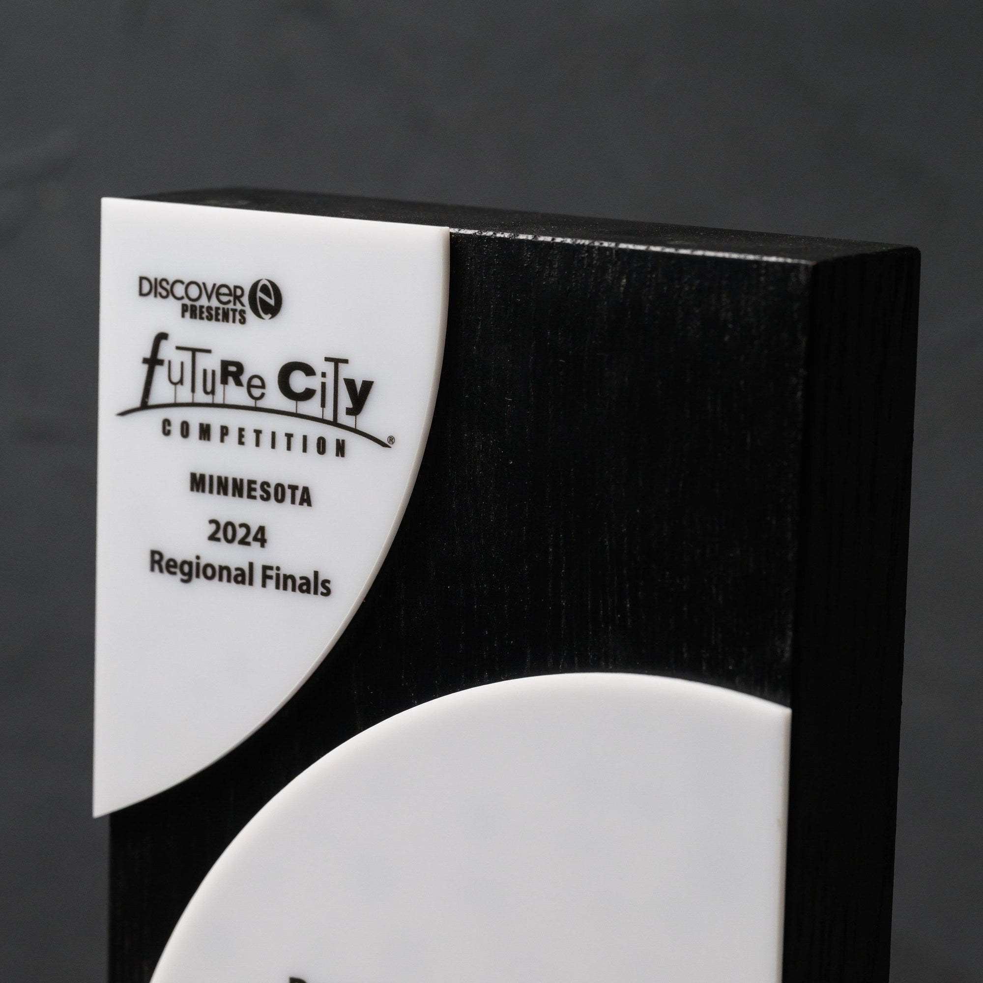 Upper white acrylic segment printed with the event logo, set against the black oak face
