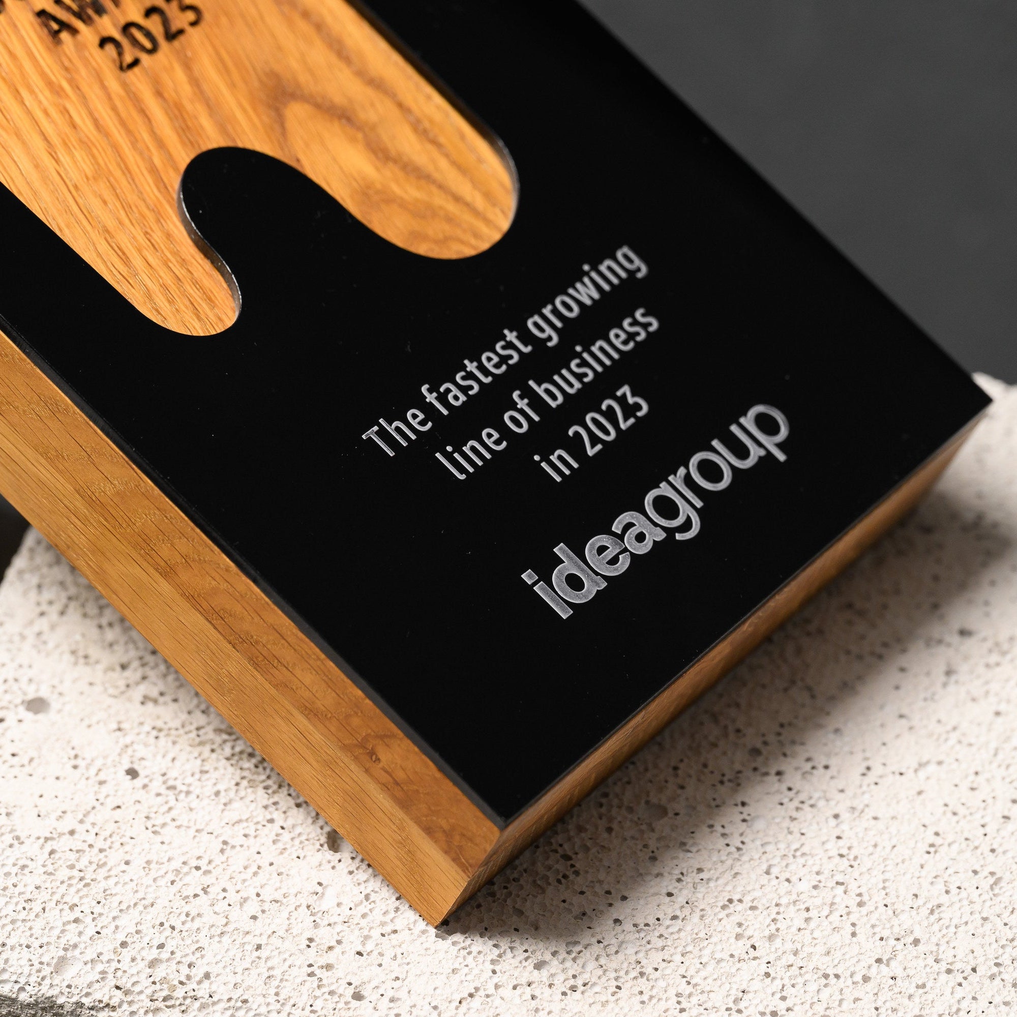 Angled close view of the engraved wording on the black acrylic beside the oak side edge