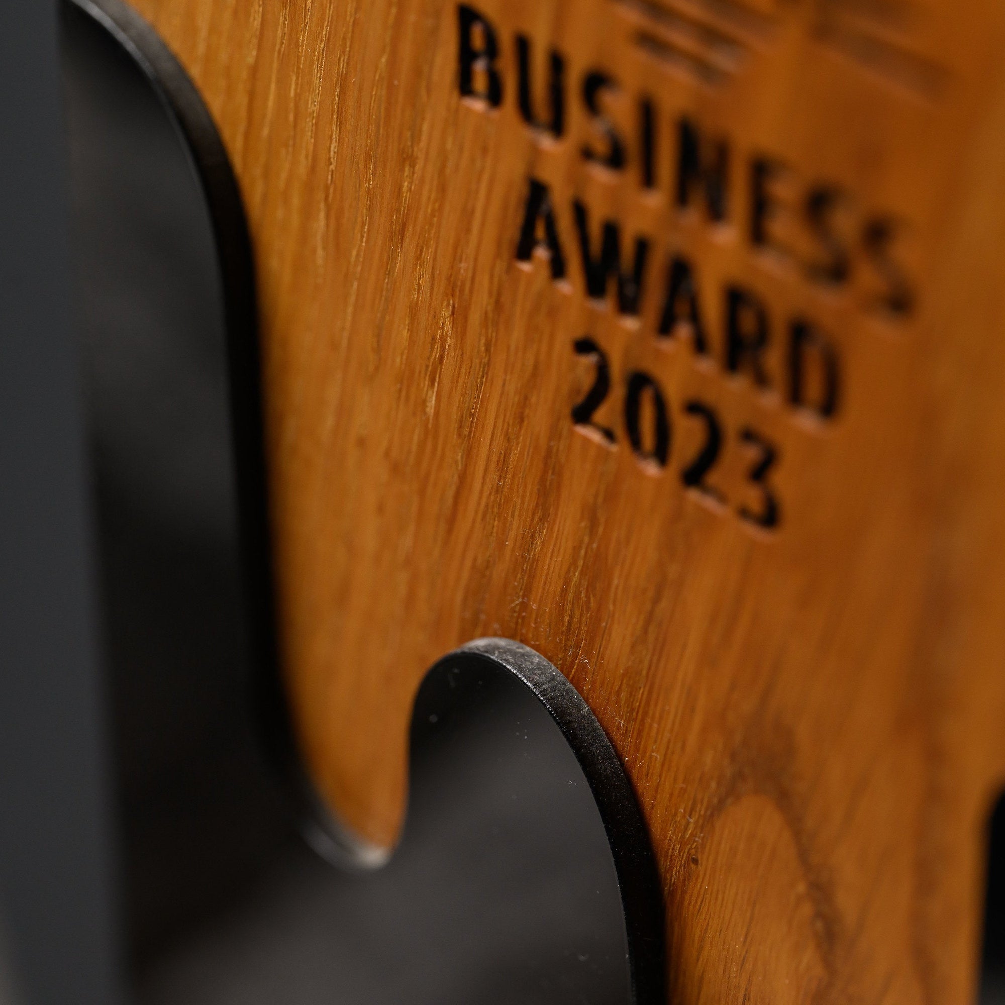 Macro of the wave-cut line where the black acrylic panel meets the engraved oak face