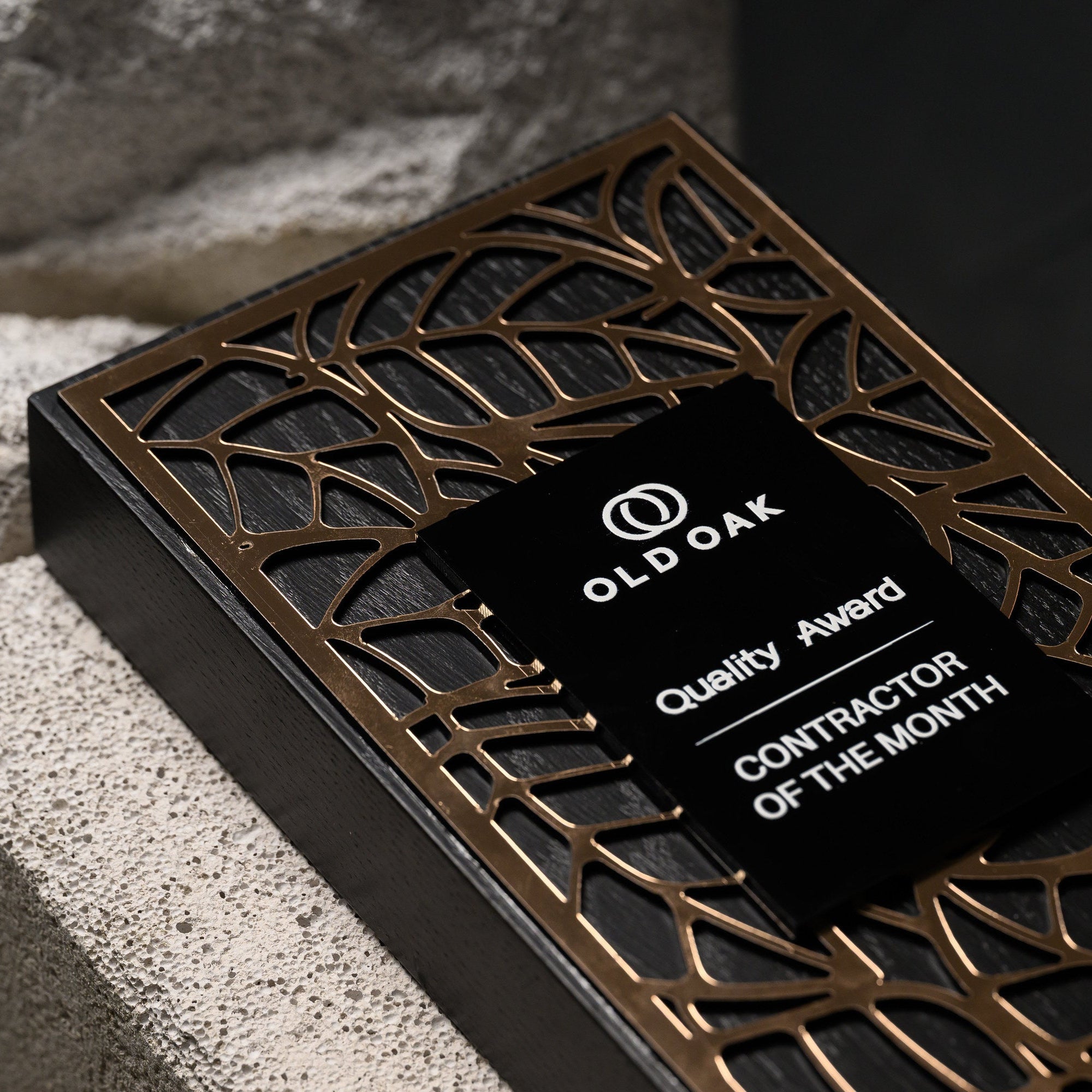 Award lying at an angle on stone, with the printed black plate set over the gold lattice