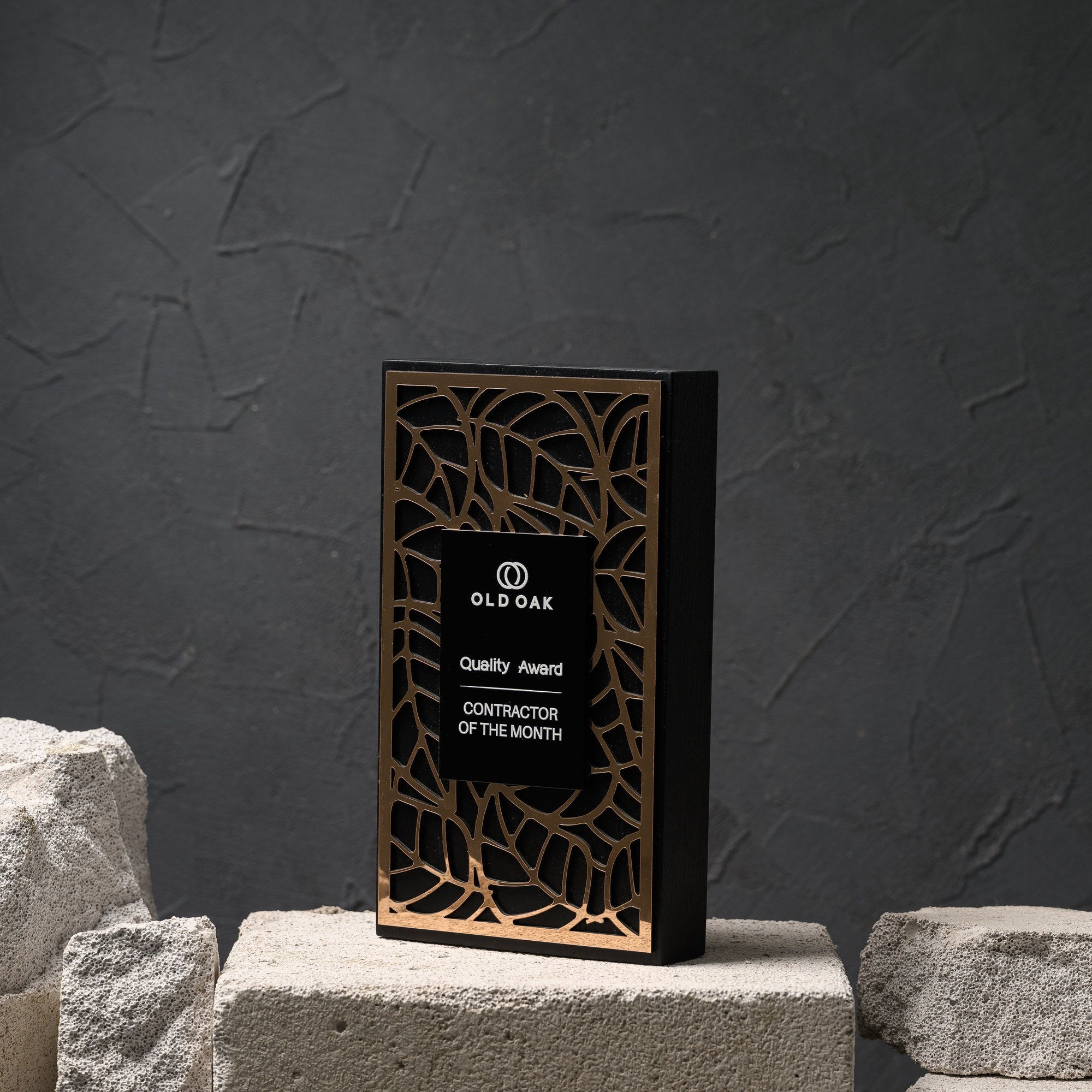 Blackened oak award with a laser-cut gold acrylic lattice, standing on a stone plinth