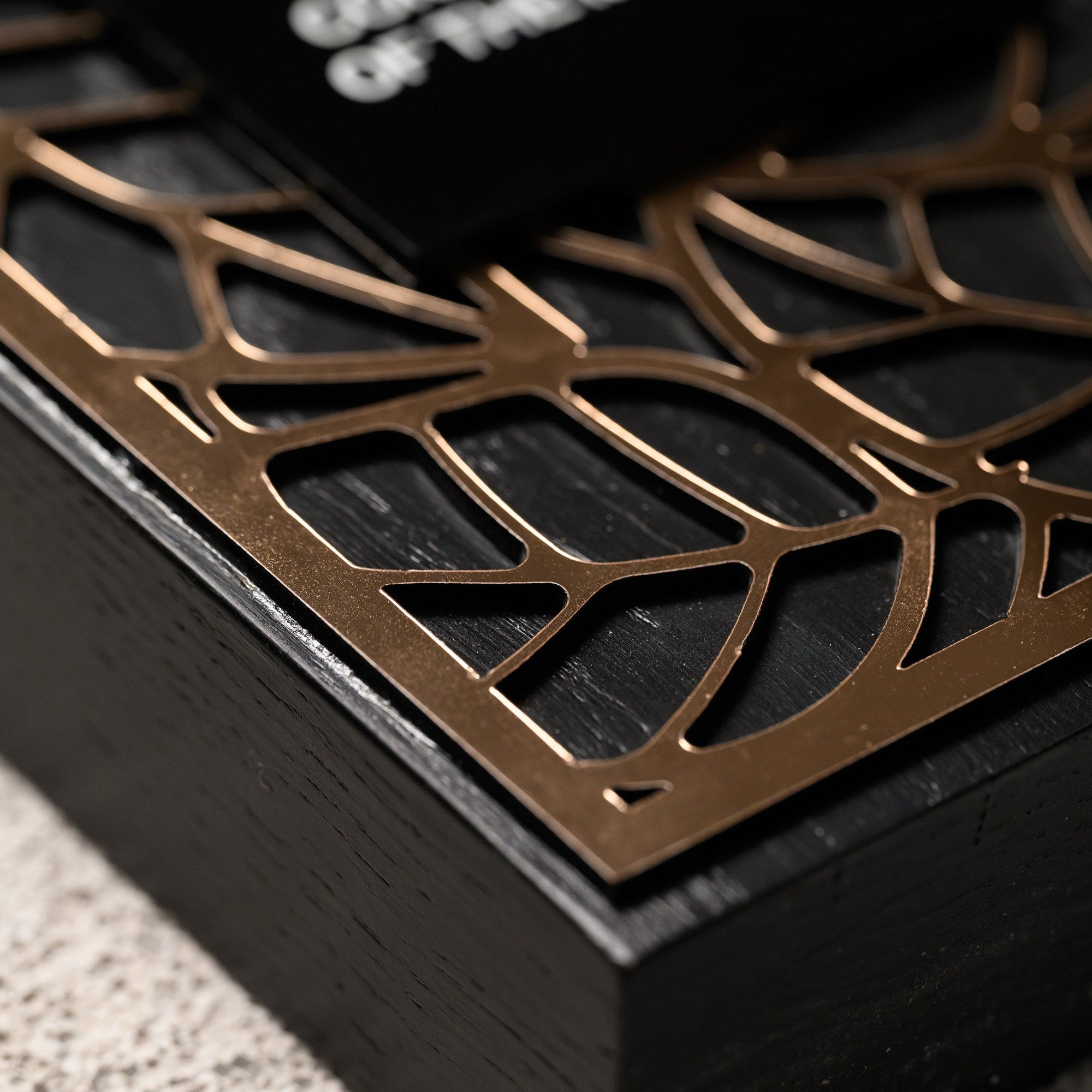 Macro of the laser-cut gold acrylic tracery lying over the blackened oak surface
