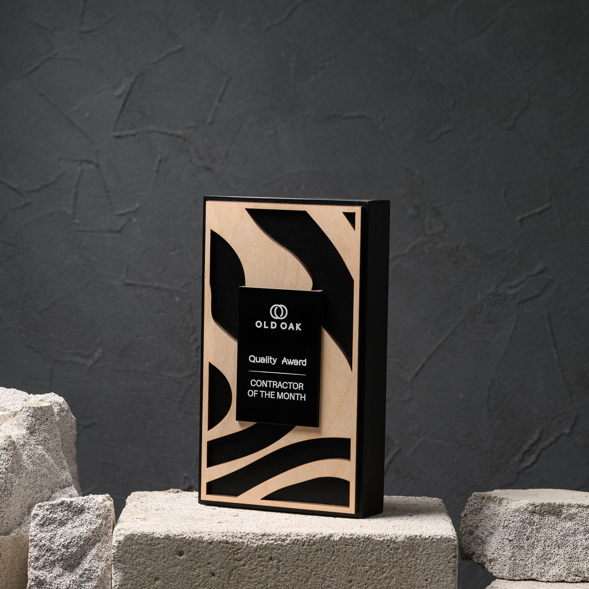 Black oak award plaque with a laser cut plywood front panel standing on a pale stone block