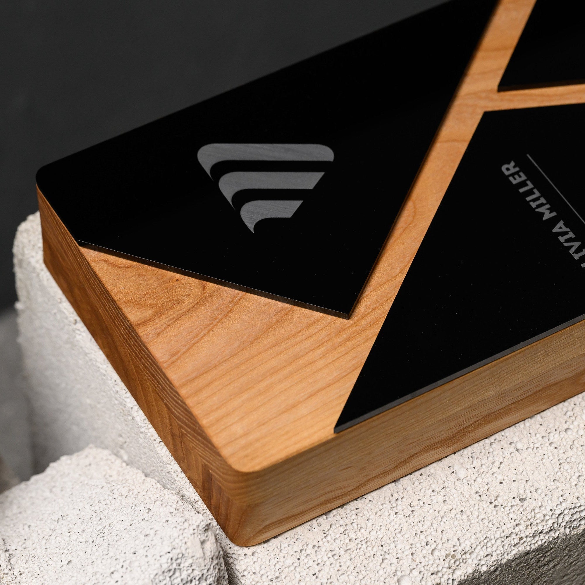 Angled close view of the black panel framed by oak, with the engraved emblem catching light