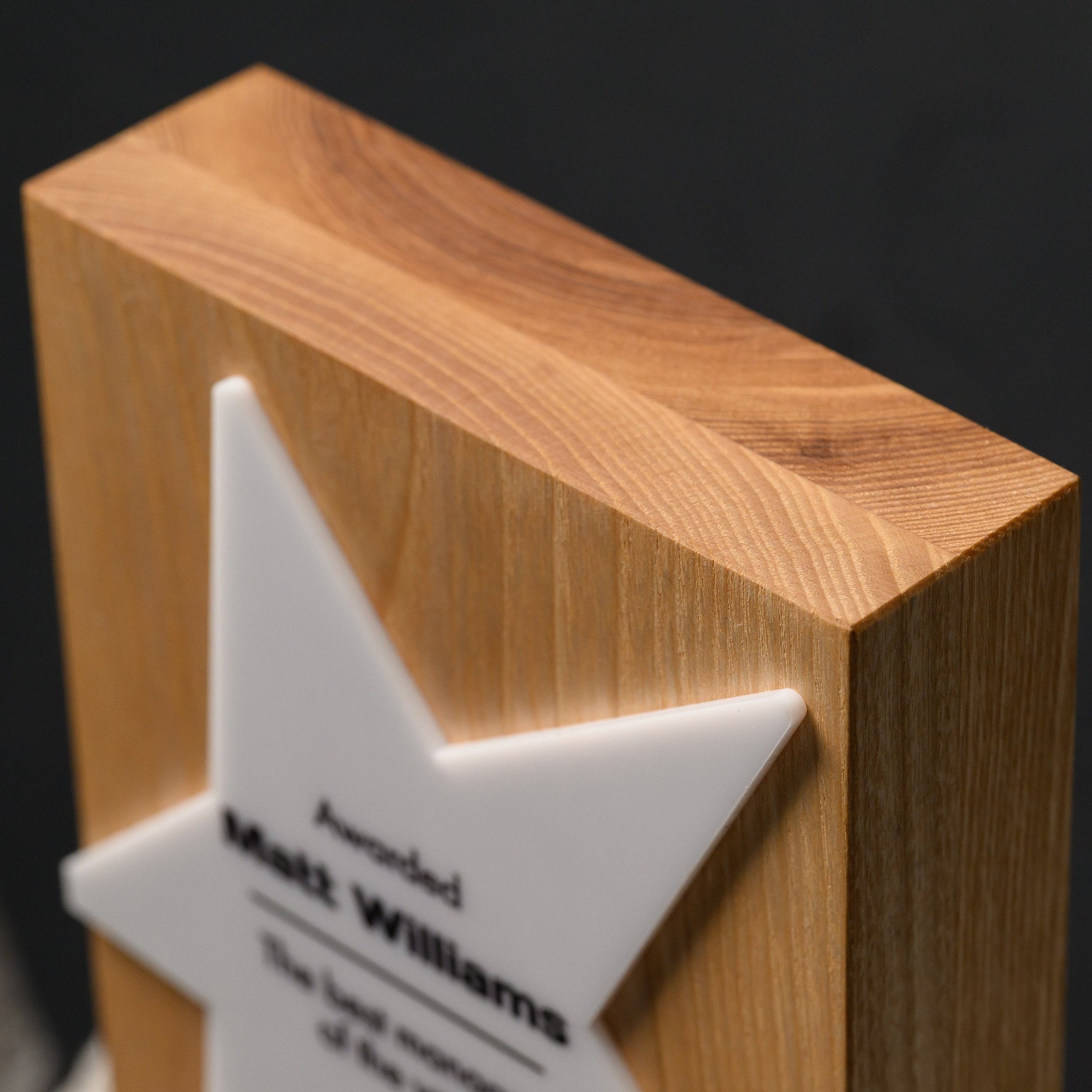 Close-up of the white acrylic star point with UV-printed black text against oak grain