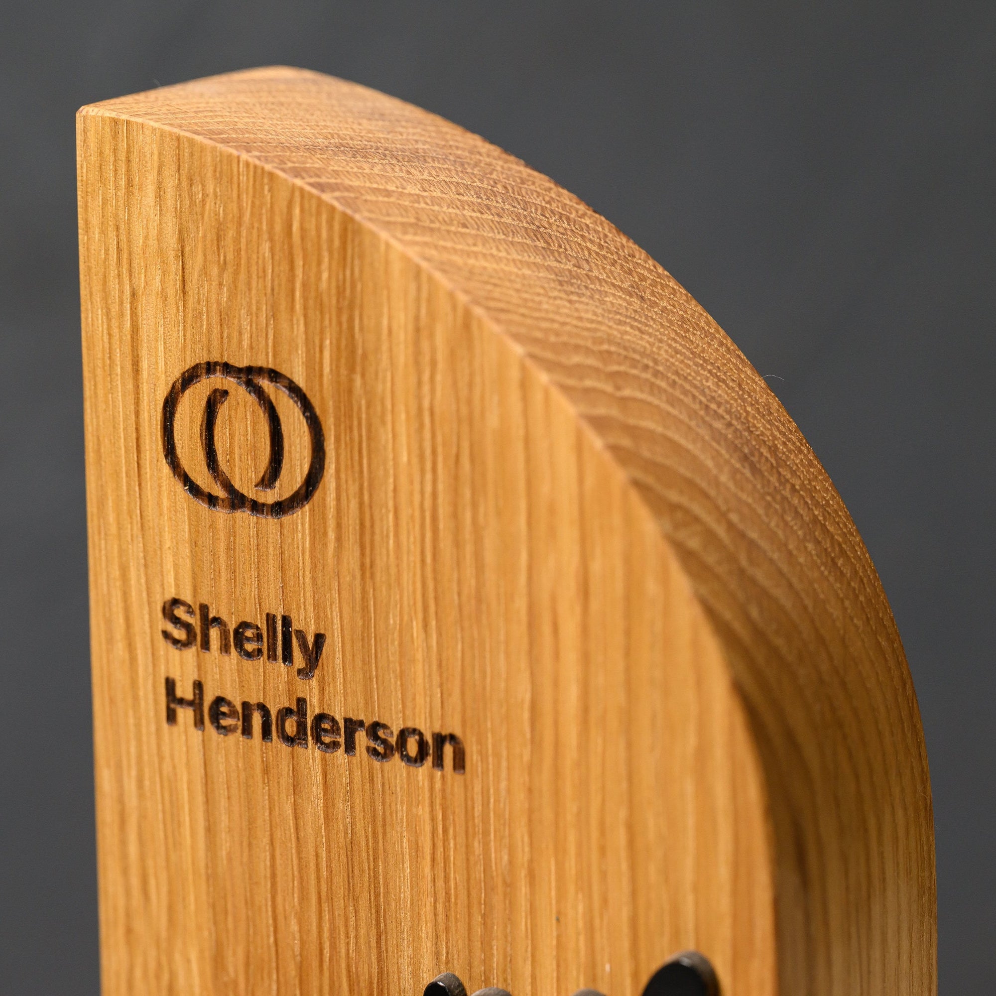 Curved top edge of the solid oak award, showing grain, thickness and the engraved panel