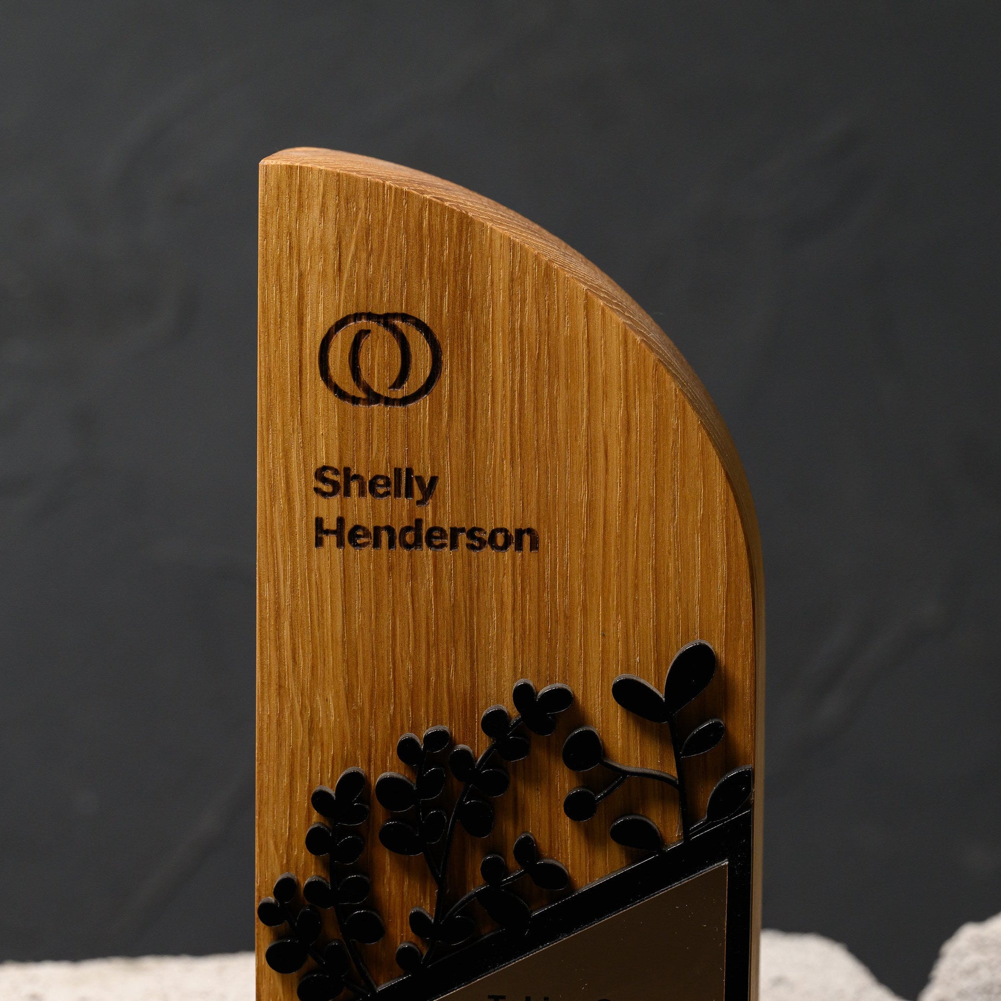 Upper section of the oak award showing laser-engraved branding above the acrylic foliage