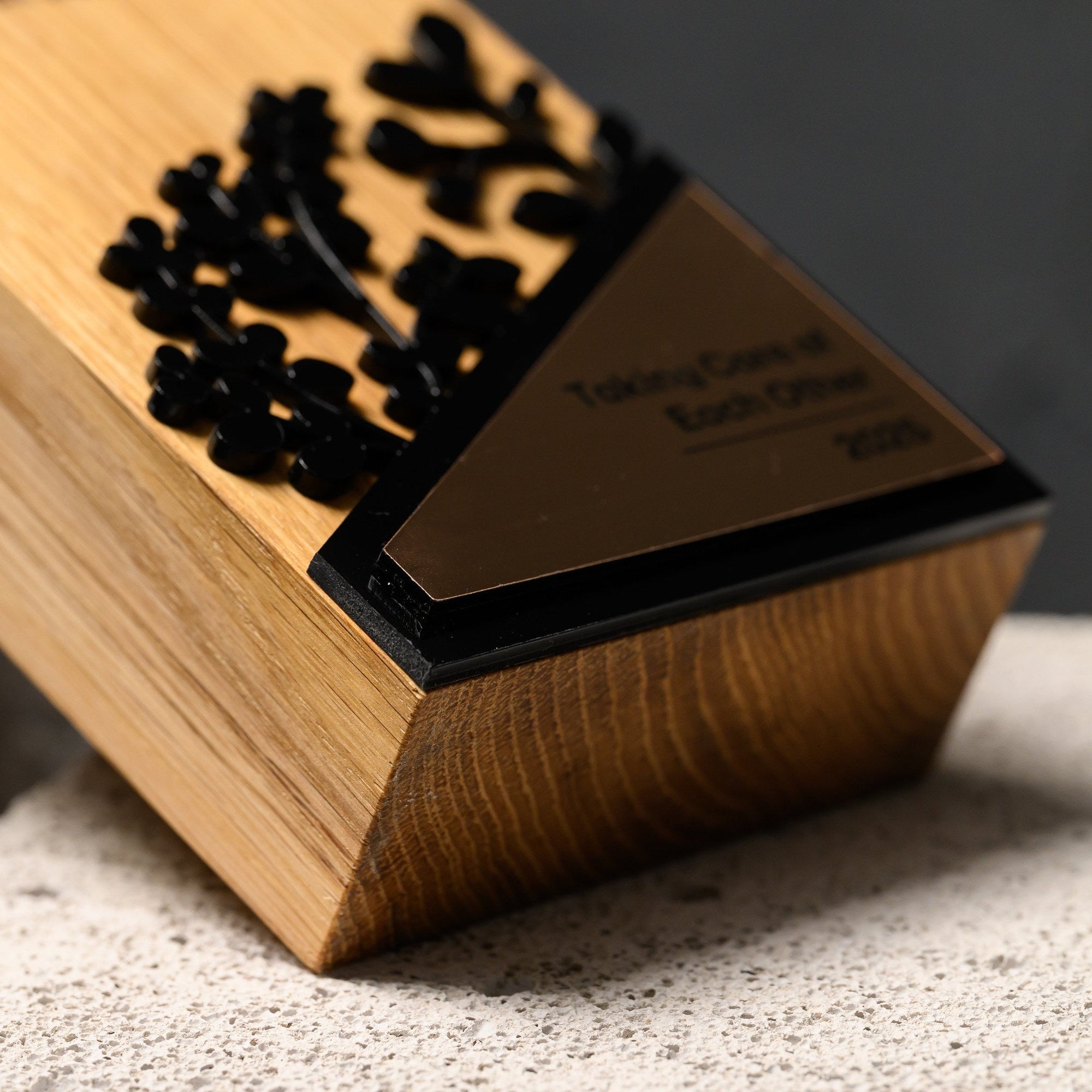 Angled close view of the black acrylic foliage meeting the gold triangular plate on oak