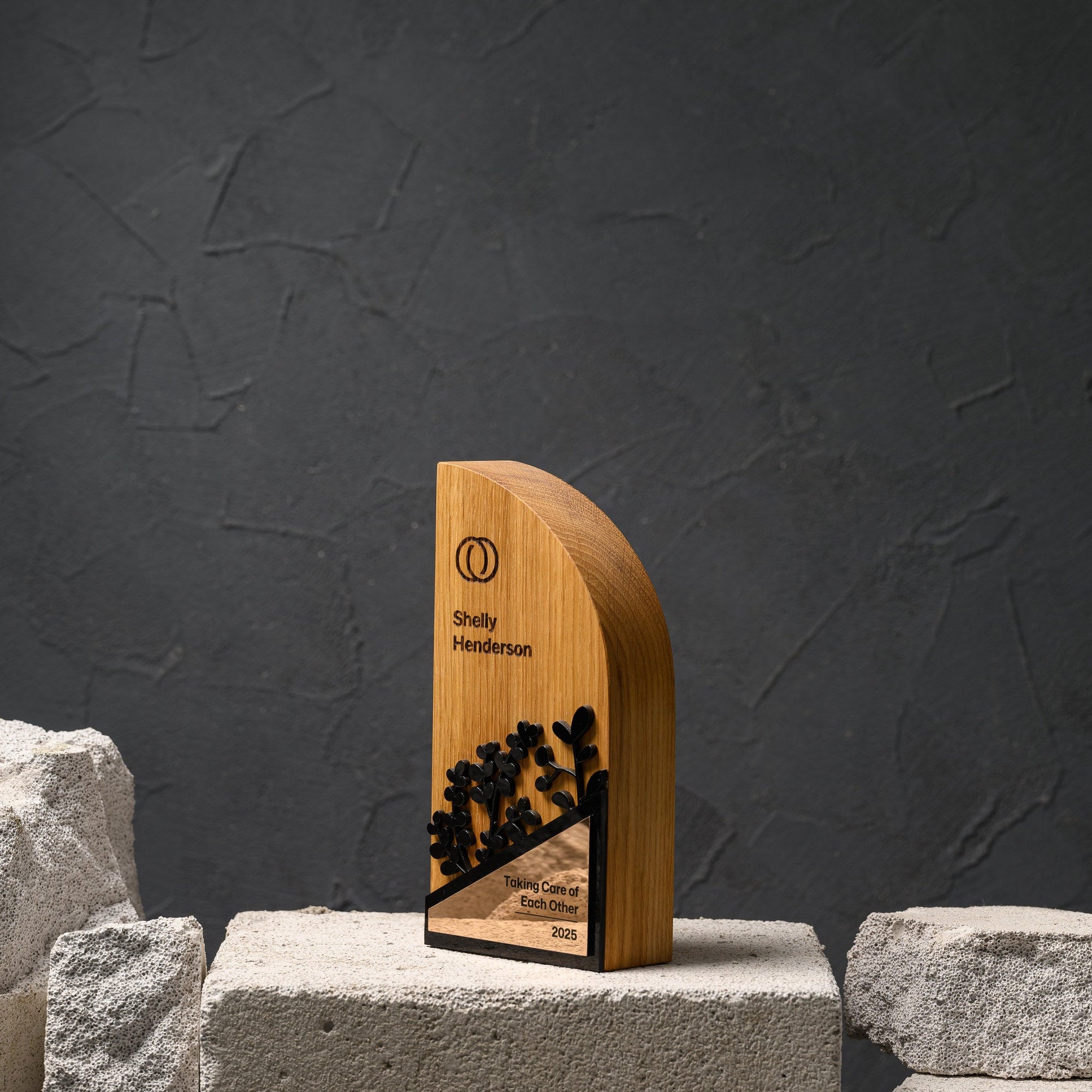 Arch-shaped oak award with black acrylic foliage and a gold mirror plate, standing on a stone plinth