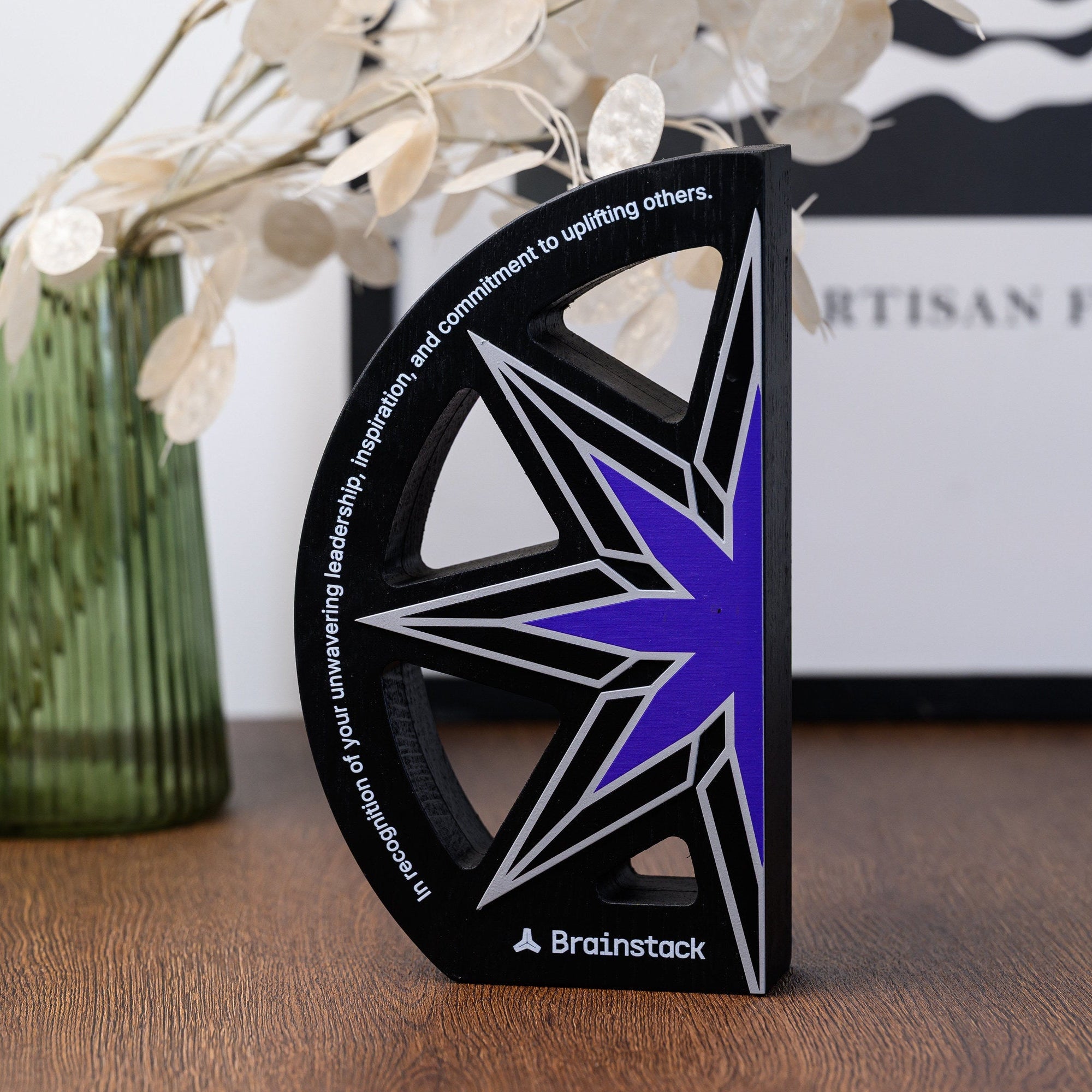 Angled view of the black arc award on a desk beside a green vase, showing the depth of the panel