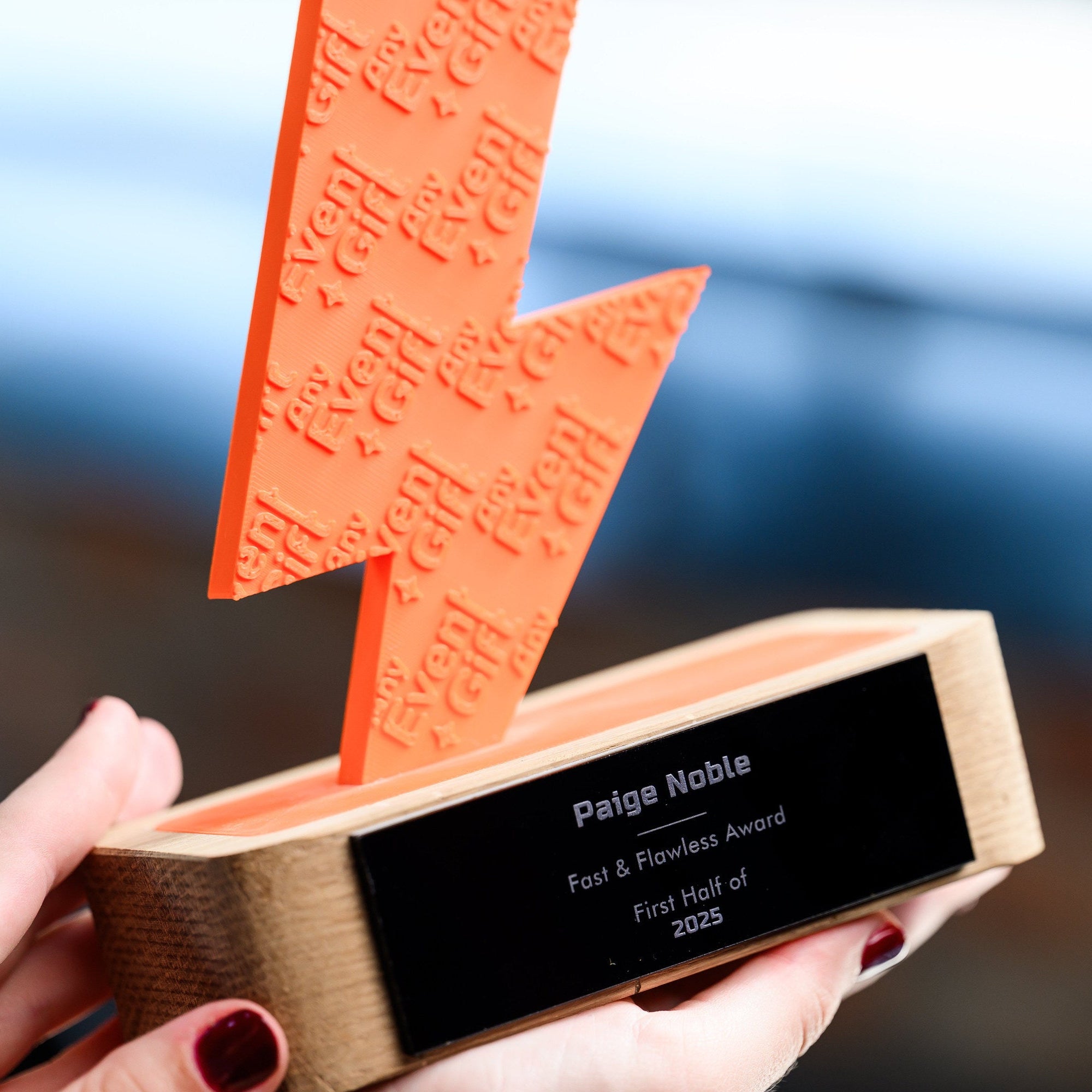 Hand holding the oak base of the trophy at an angle, with the printed figure rising above it