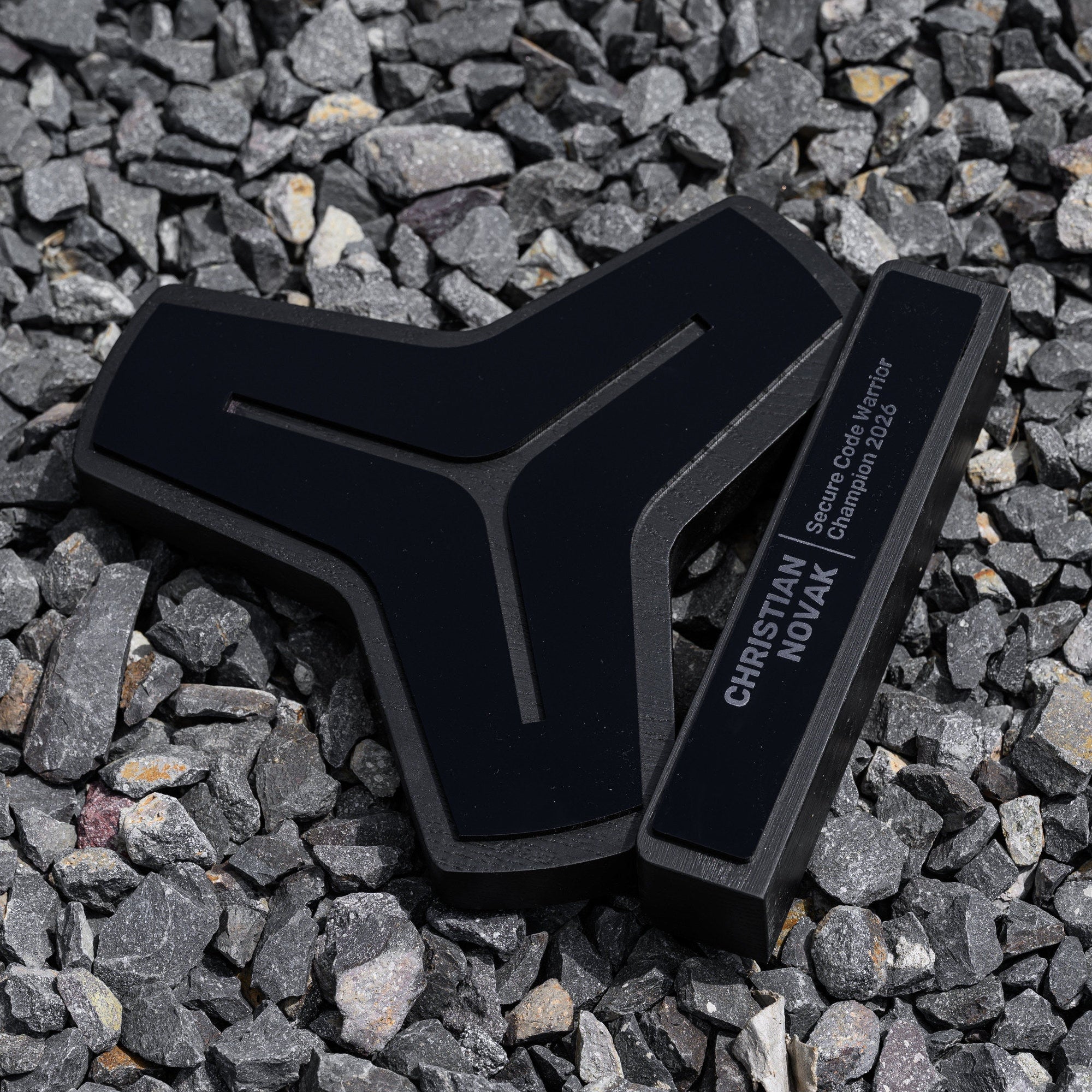 All black custom shaped award lying on grey gravel with the engraved nameplate facing the camera