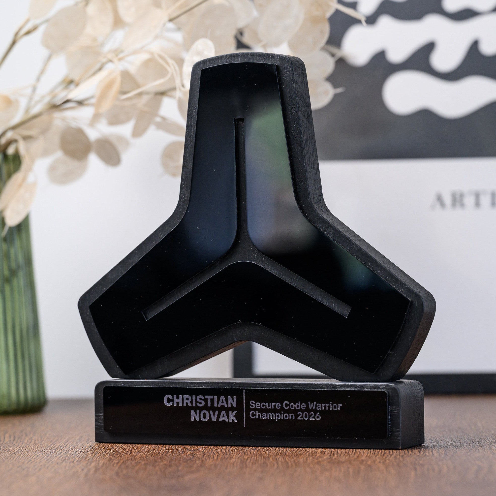 Black logo shaped trophy on a desk with dried flowers and a framed print in the background