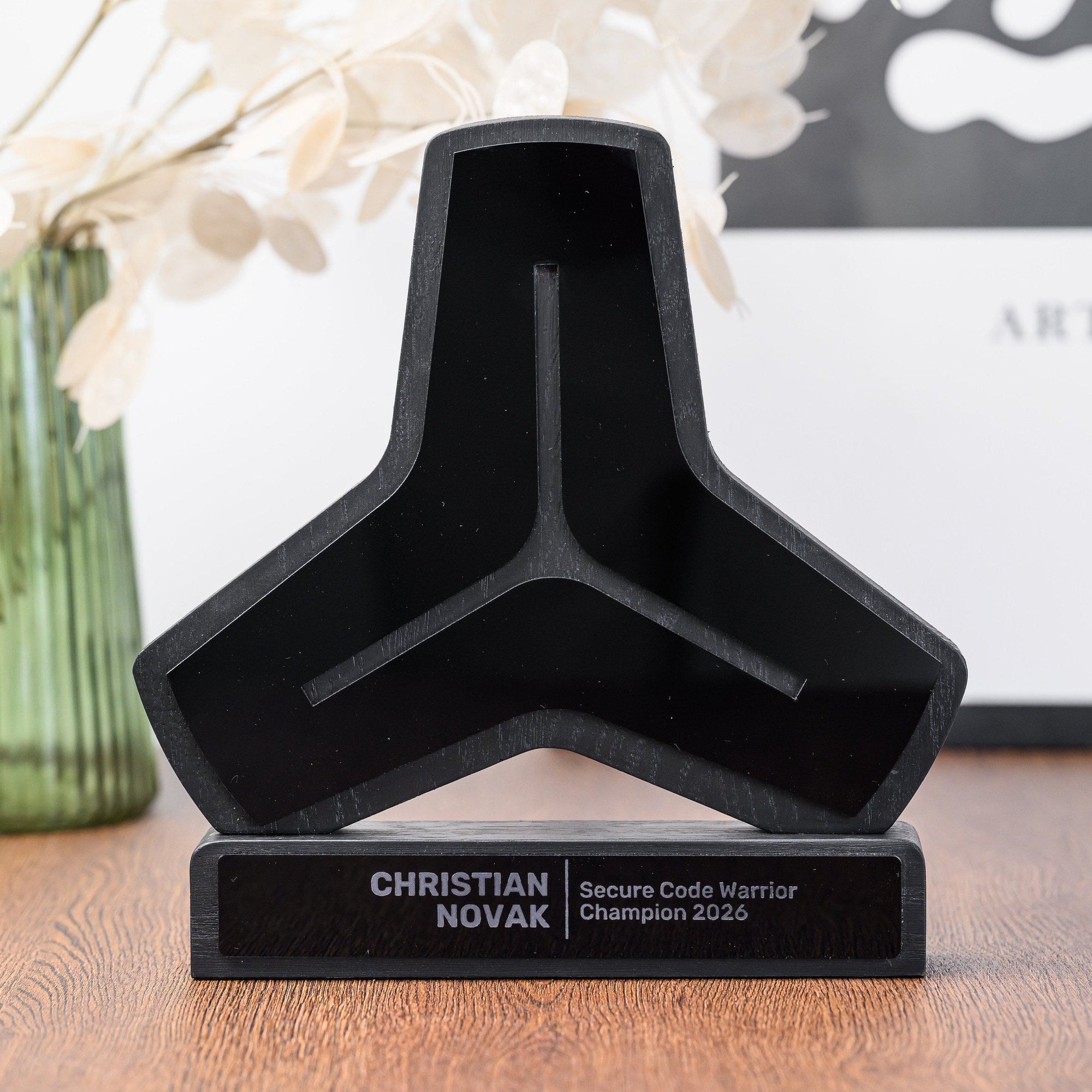 Custom logo shaped corporate award in black oak and acrylic standing on a wooden desk beside a vase