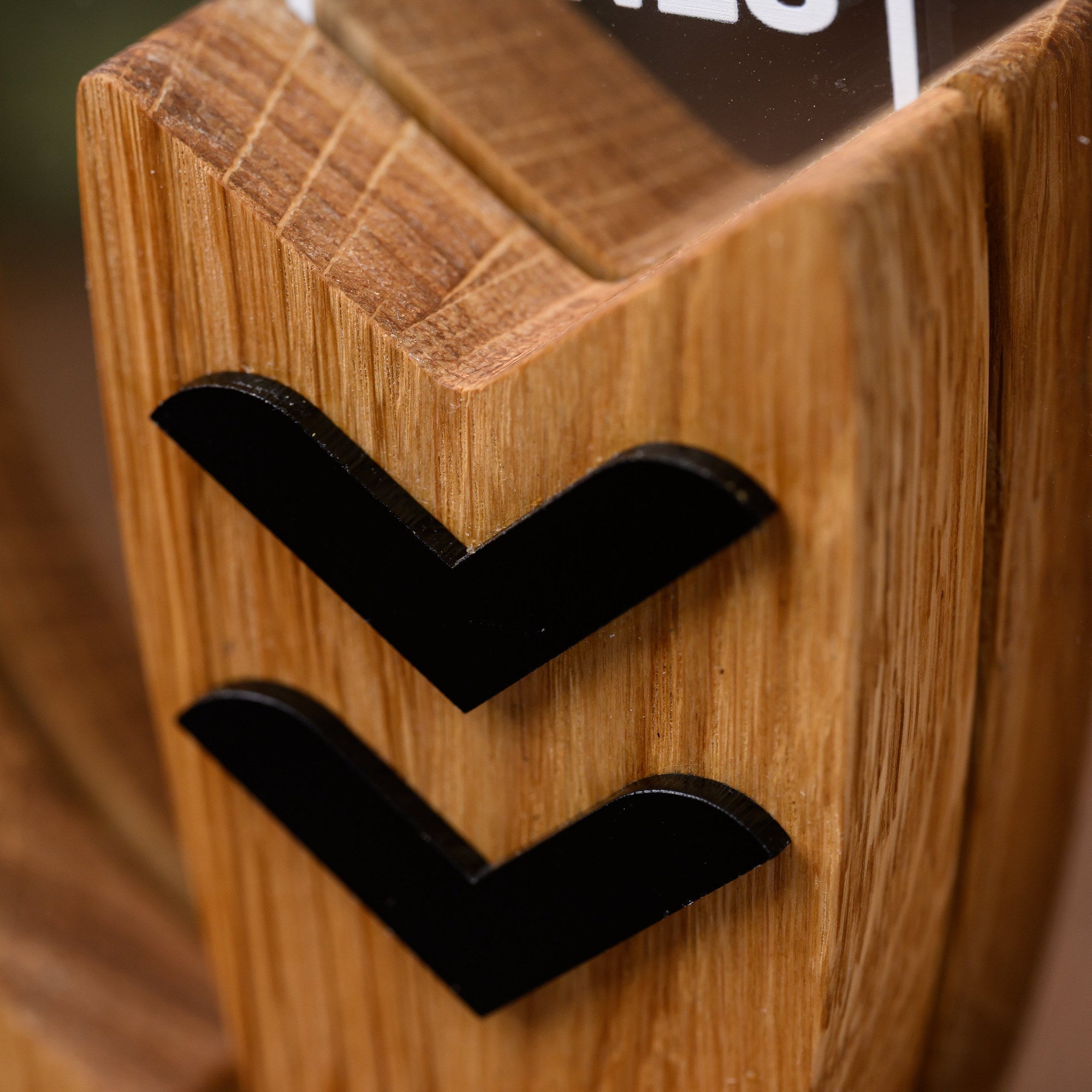 Two black acrylic chevrons inlaid into the oak surfboard element of the custom surf trophy, up close