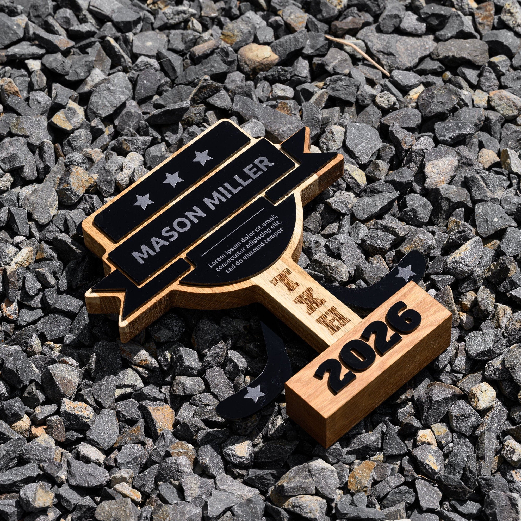Oak and acrylic hockey trophy lying on grey gravel with the engraved name banner facing upwards